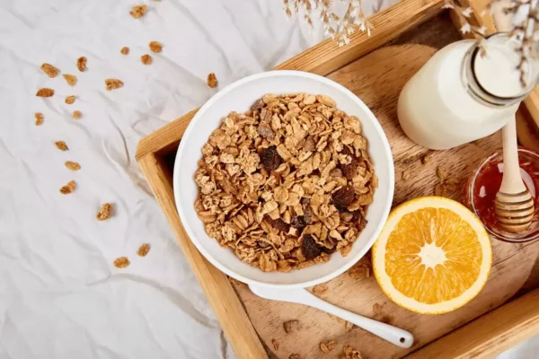 süt ve portakalla birlikte tepsiye yerleştirilmiş bir kase müsli